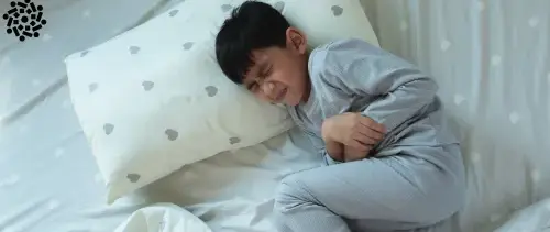 Criança deitada na cama com dor abdominal, um dos sintomas de gastrite